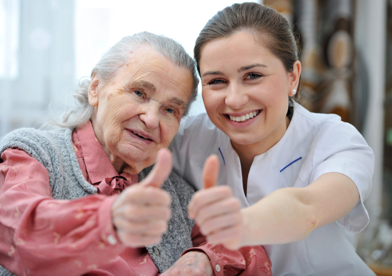 femme âgée avec aide soignantes sourient et montrent leur pouce en l'air